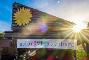 Holzhaus mit Sonne und Banner SolarINI Lauenburg