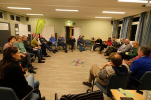 Eine große Gruppe von Menschen sitzt im Kreis und diskutiert. 